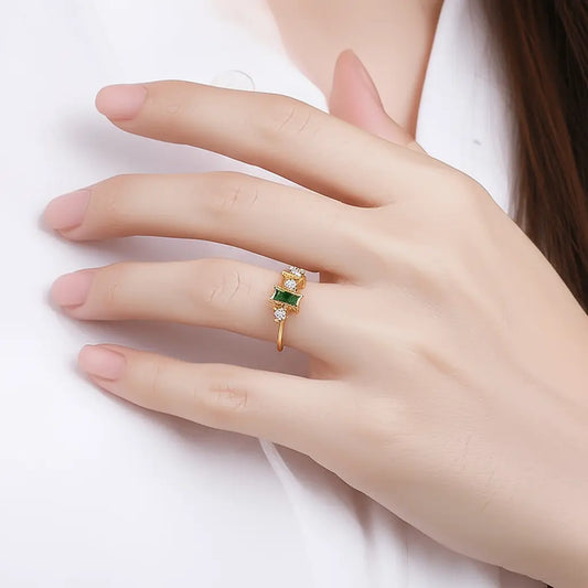 Gold ring with a green gemstone on a hand against a white background