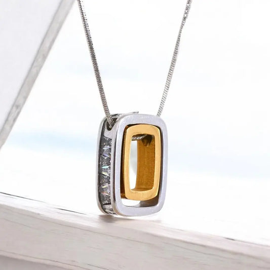 Gold and silver pendant on a chain against a blurred outdoor background