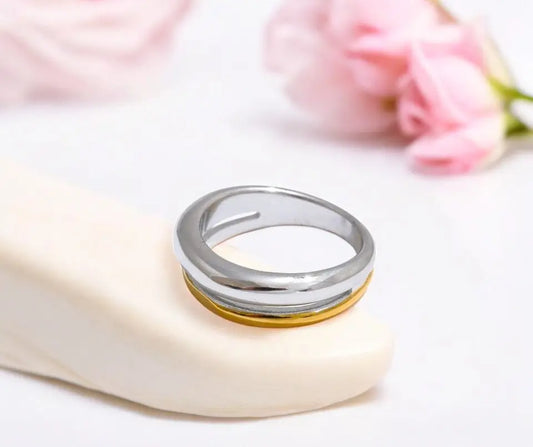 Two rings, one silver and one gold, on a white surface with pink flowers in the background.