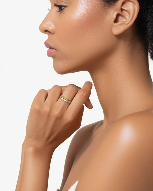 Close-up of a woman's neck and hand with a ring on a light gray background